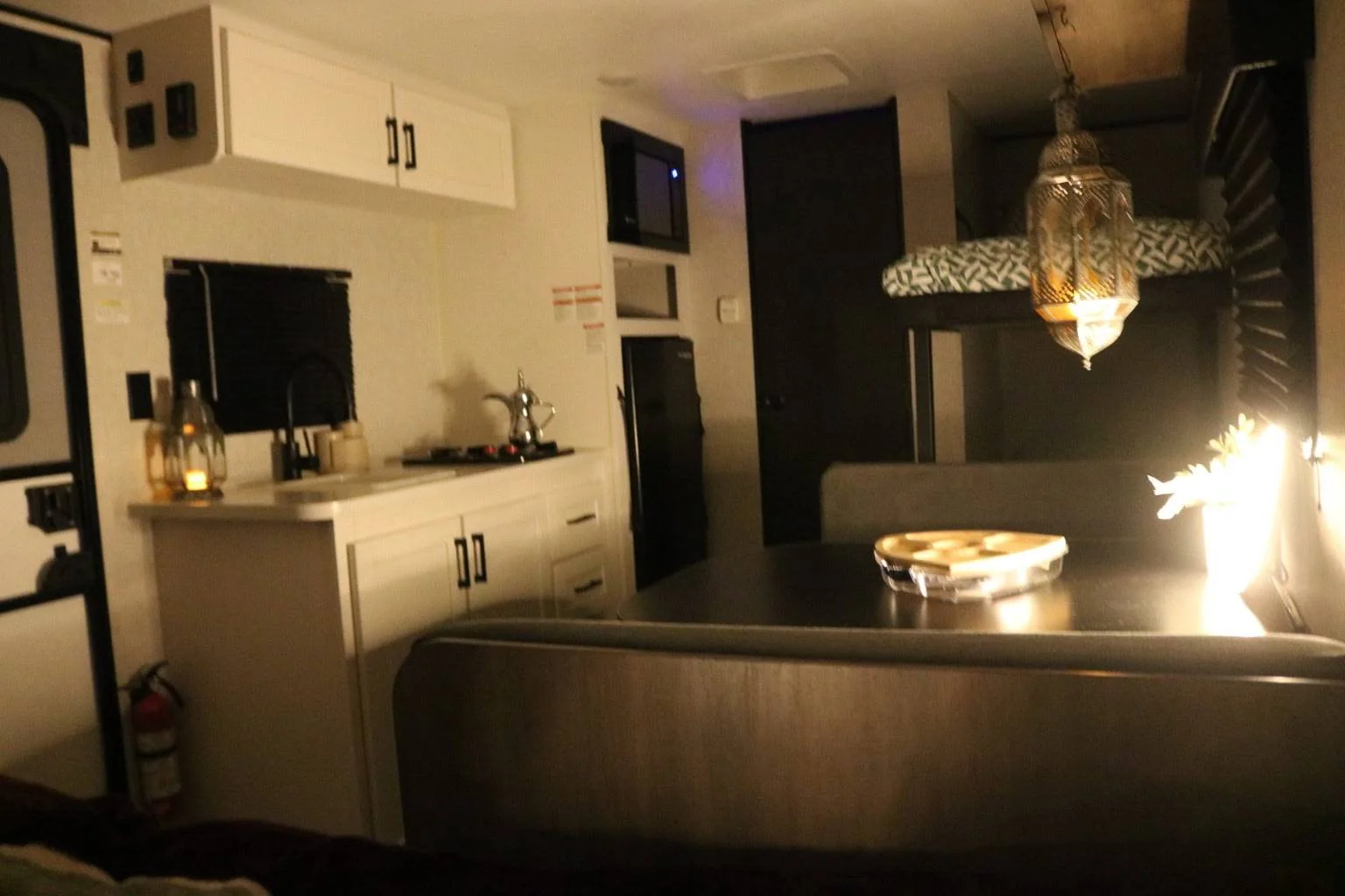 JayCation interior with the kitchen, dining table, and bunk beds lit for the evening