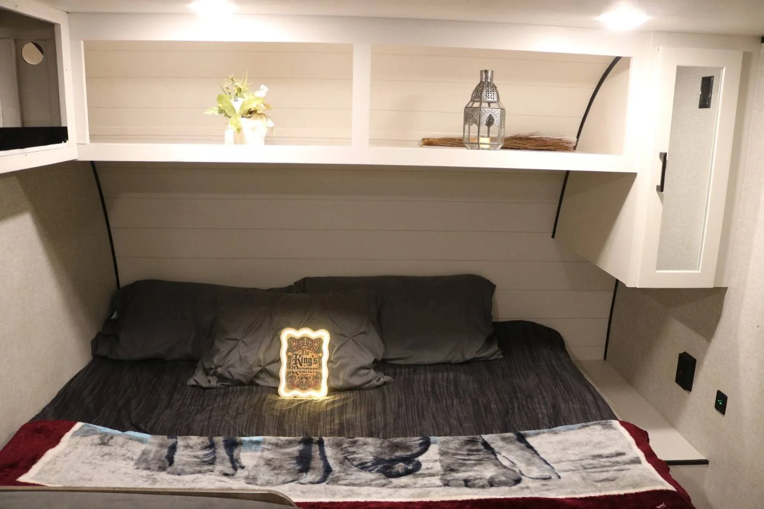 The Basecamp sleeping area with a made bed, reading lights and overhead shelving